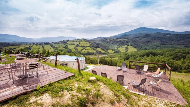 A wooden deck with outdoor seating and a view of rolling hills and mountains. - Società Agricola Cacigolara (Borgo Val di Taro)