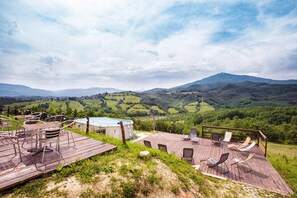 A wooden deck with outdoor seating and a view of rolling hills and mountains. - Società Agricola Cacigolara (Borgo Val di Taro)