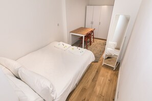 Une petite chambre à coucher, bien rangée, avec un lit simple, une table en bois et une chaise.