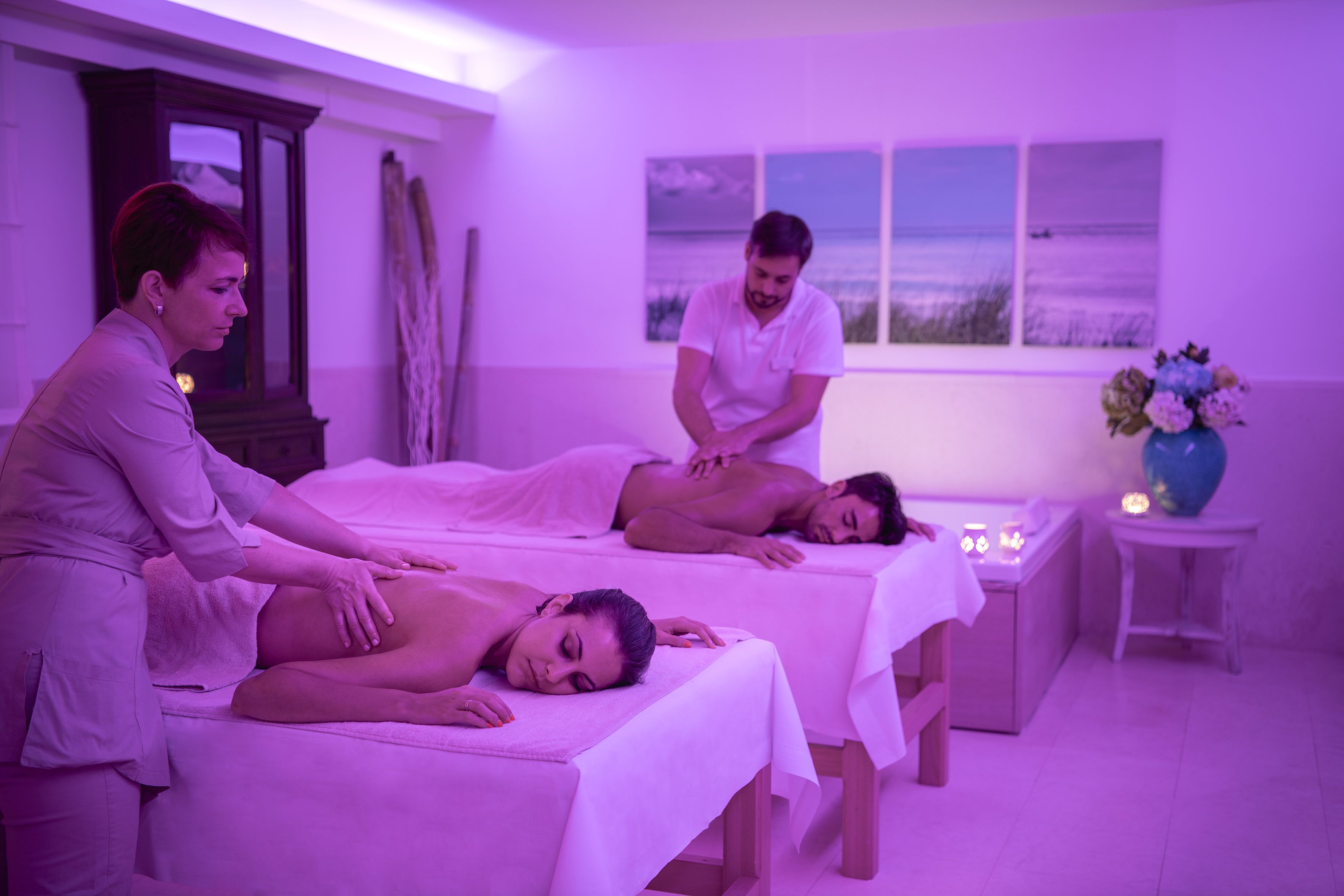 Una stanza spa con tre lettini da massaggio, un armadietto in legno e una finestra vista spiaggia.