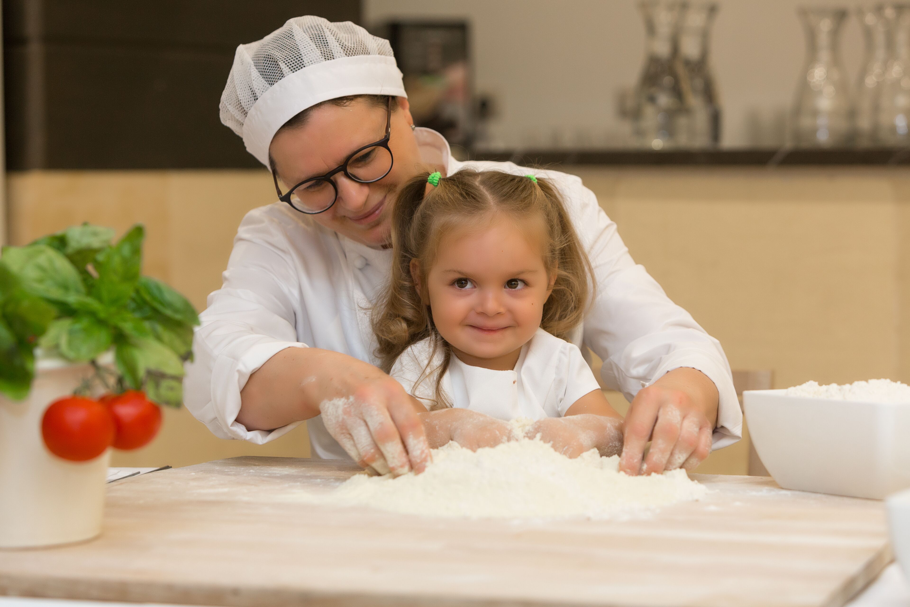 A person and a child kneading dough on a kitchen counter.