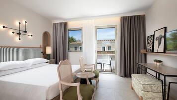 Una camera d'albergo con un letto, due sedie, un tavolino, una panca, una scrivania e vista dalla finestra.