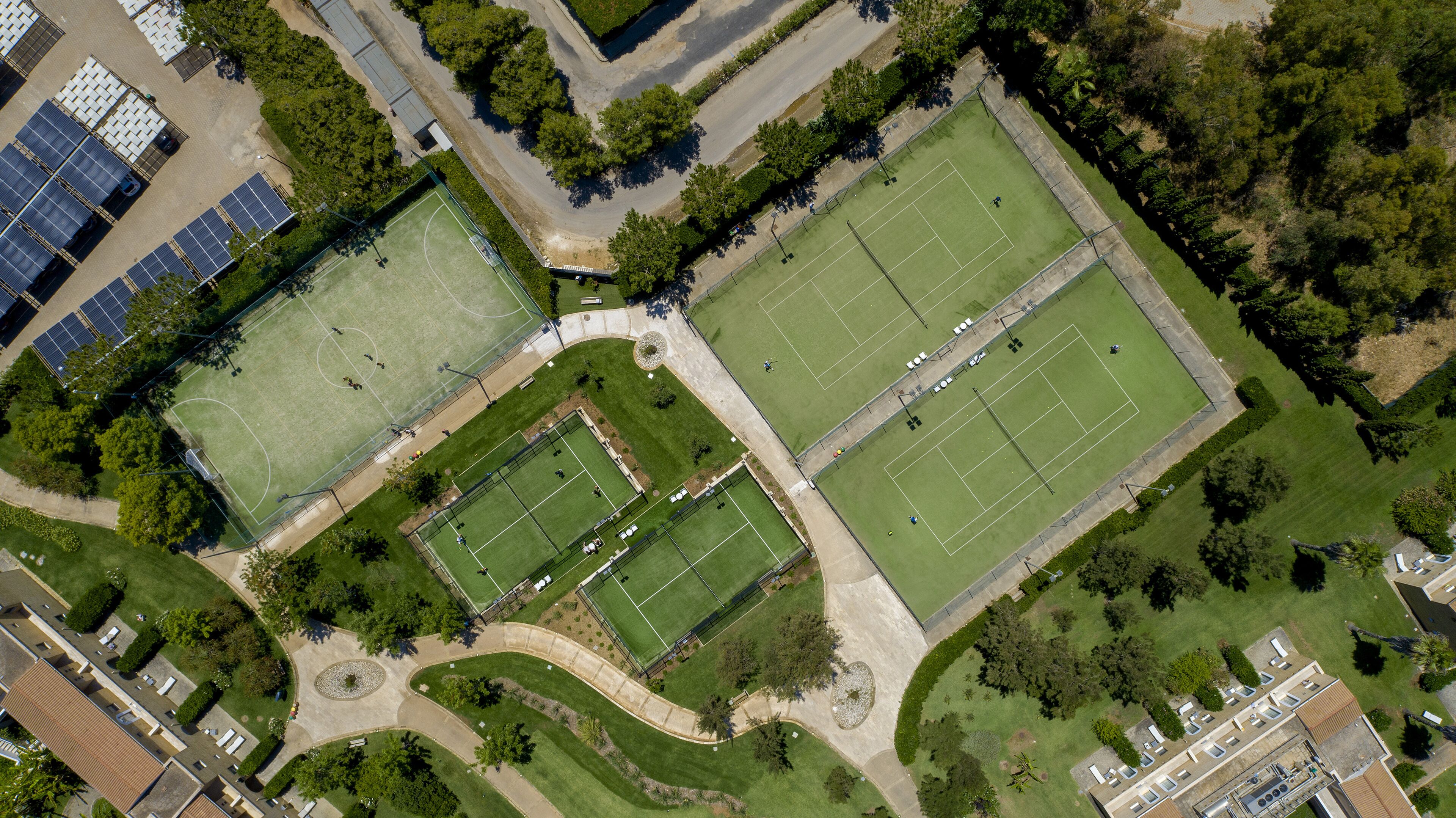 Vista aerea di un complesso sportivo con diverse piste da tennis, un'area di parcheggio e pannelli solari.
