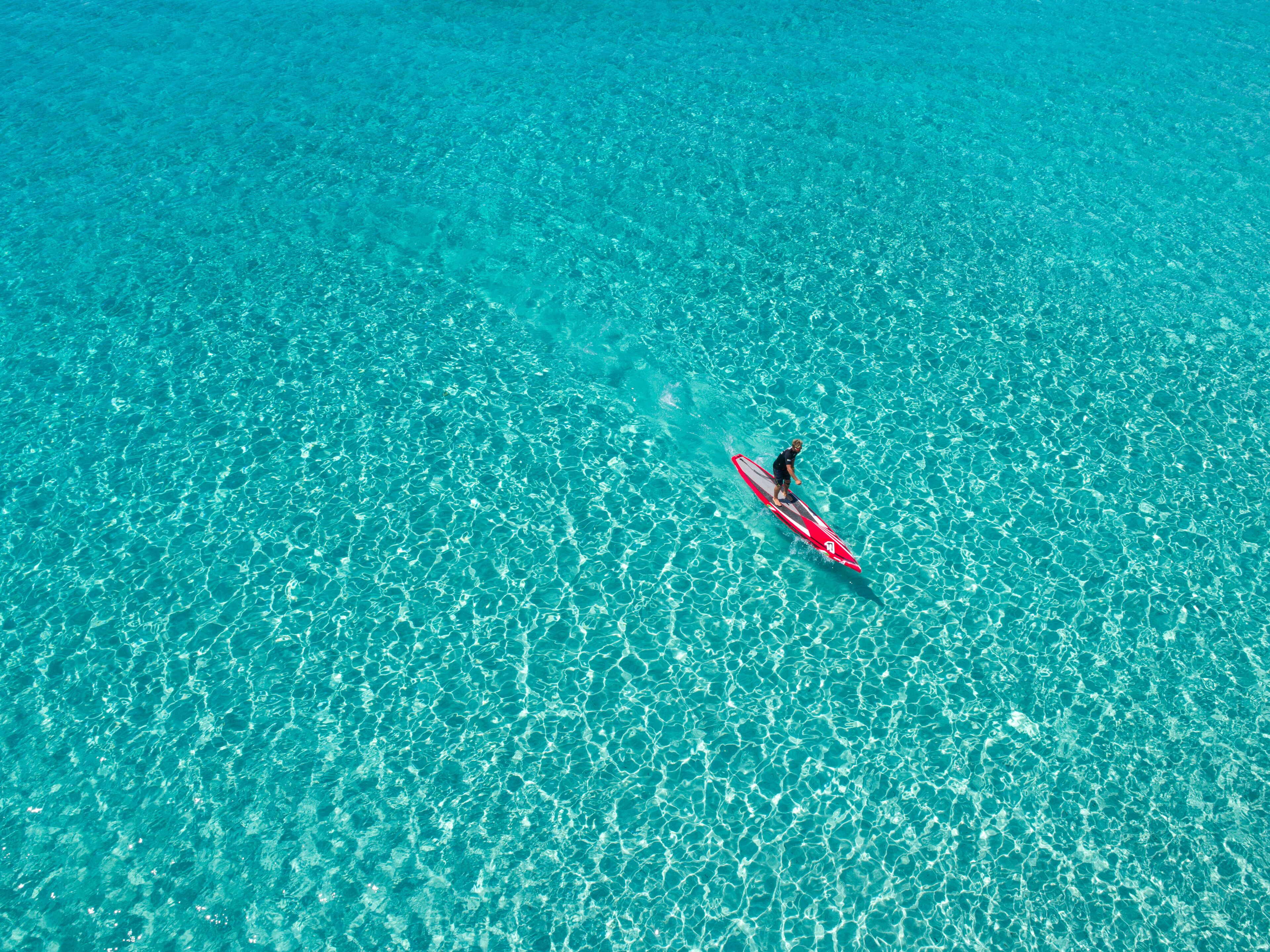 Eine Person steht auf einem roten Stand-Up-Paddleboard in klarem, türkisblauem Wasser.