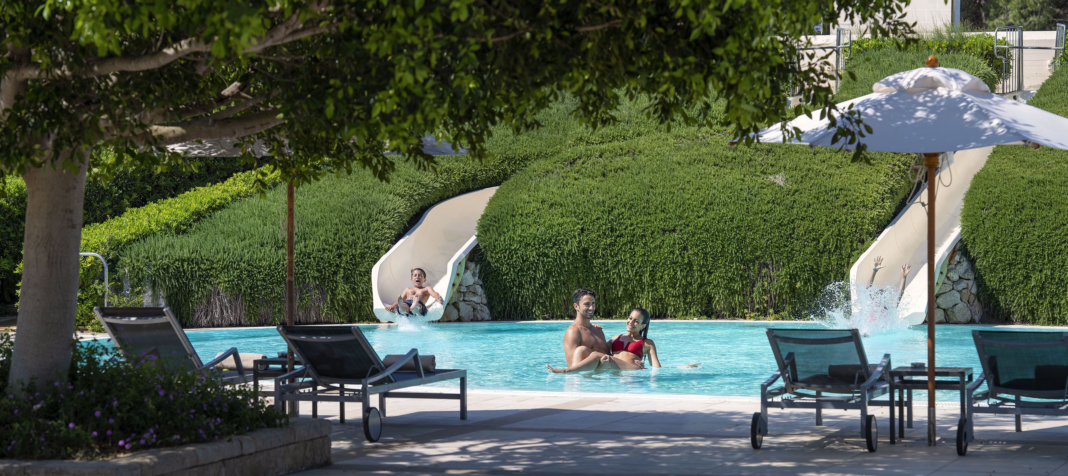 Una piscina con scivoli, sdraio e ombrelloni.