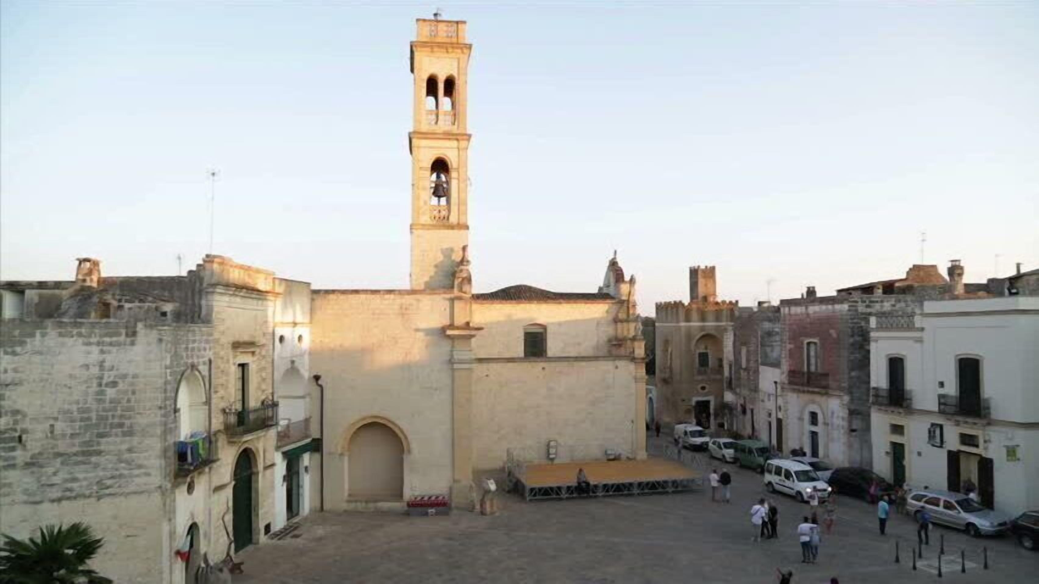 A square with a central tower, surrounded by buildings with arched doorways and a paved ground.