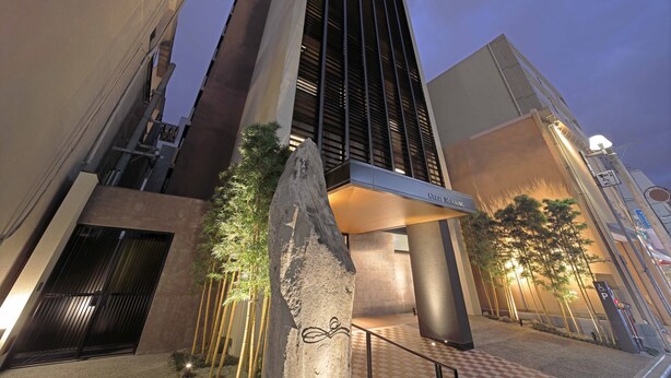 Un edificio moderno con una entrada destacada, pilares grandes y un patrón de suelo a cuadros.