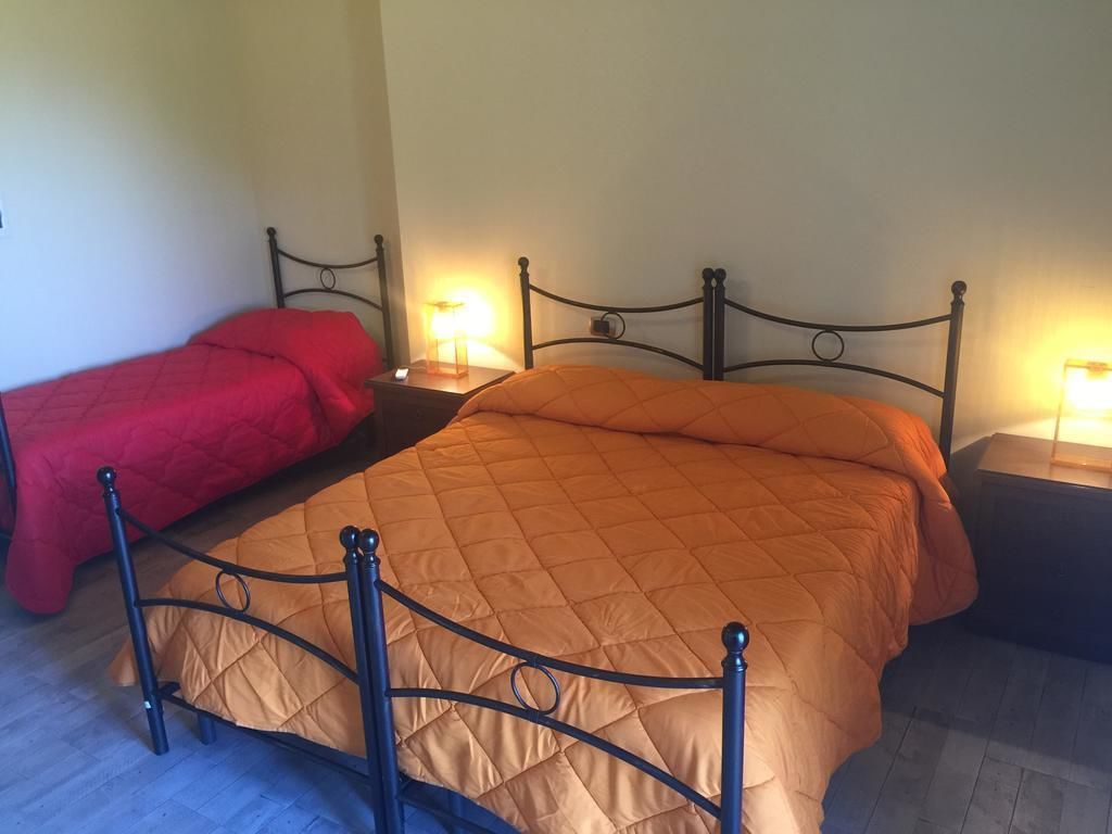 A double bed with a metal frame and a quilted orange bedspread. There are two bedside tables with lamps, and a red bedspread is visible on the left.