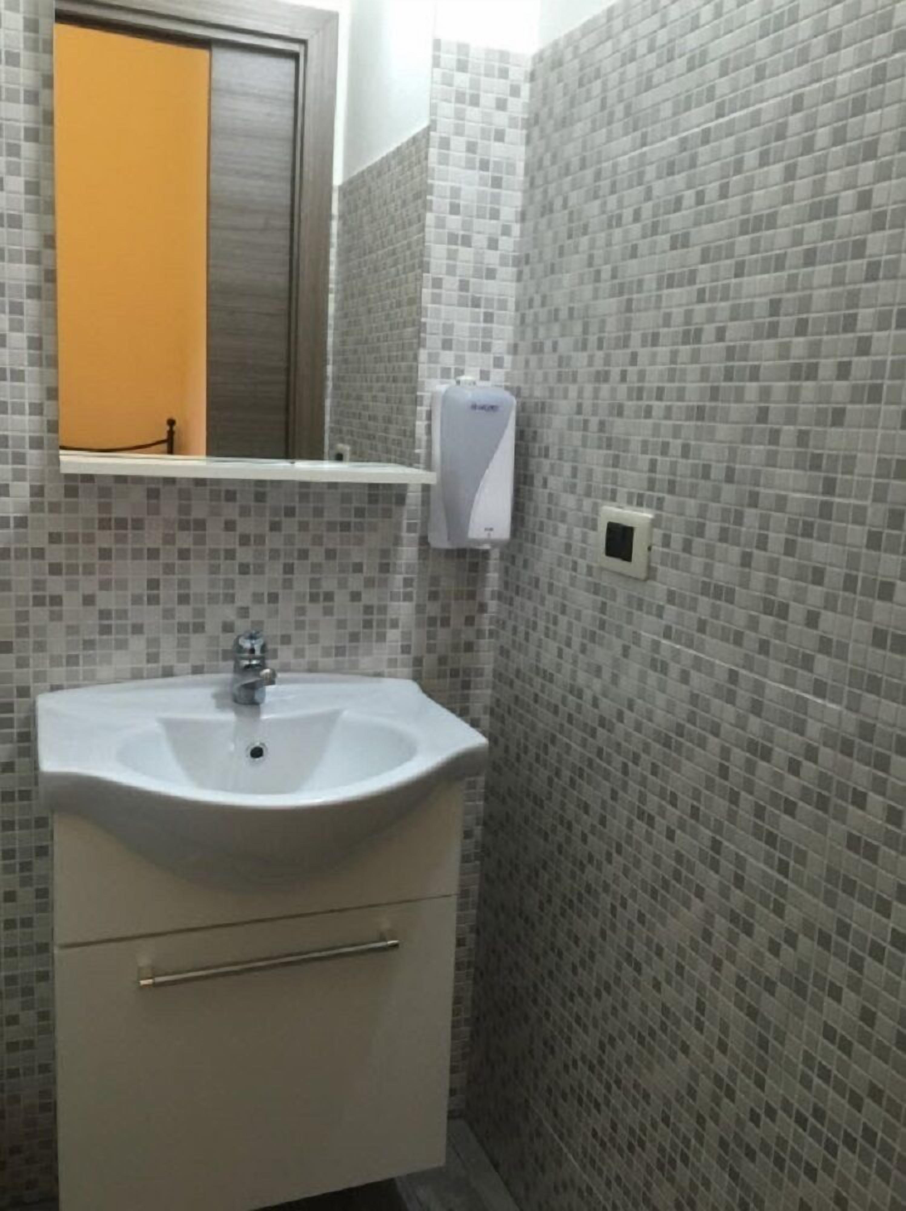 A bathroom with a white sink, a mirror, and a soap dispenser.