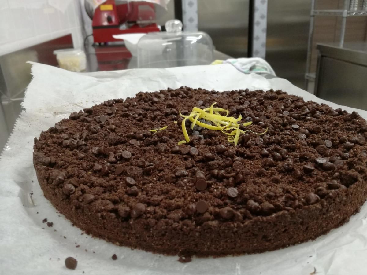 En chokoladekage med chokoladechips og et gult citronskalpynt på et stykke hvidt papir på et bord.