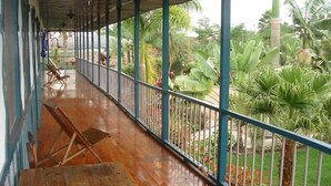 A covered balcony with wooden flooring, metal railings, and a view of tropical vegetation. - On Vacation Karlaka (Roncesvalles)