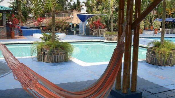 A pool area with a hammock, potted plants, and a blue umbrella. - On Vacation Karlaka (Roncesvalles)