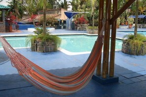 Un espace piscine agrémenté d’un hamac, de plantes en pot et d’un parasol bleu.