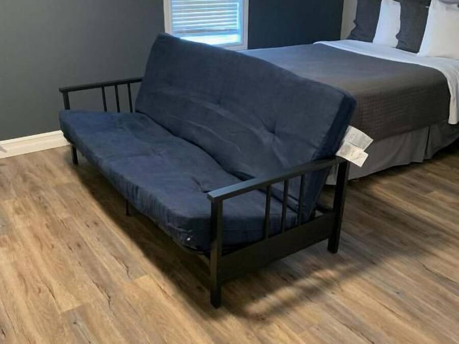 A room with a dark blue sofa, a bed with white bedding, and a window with blinds.