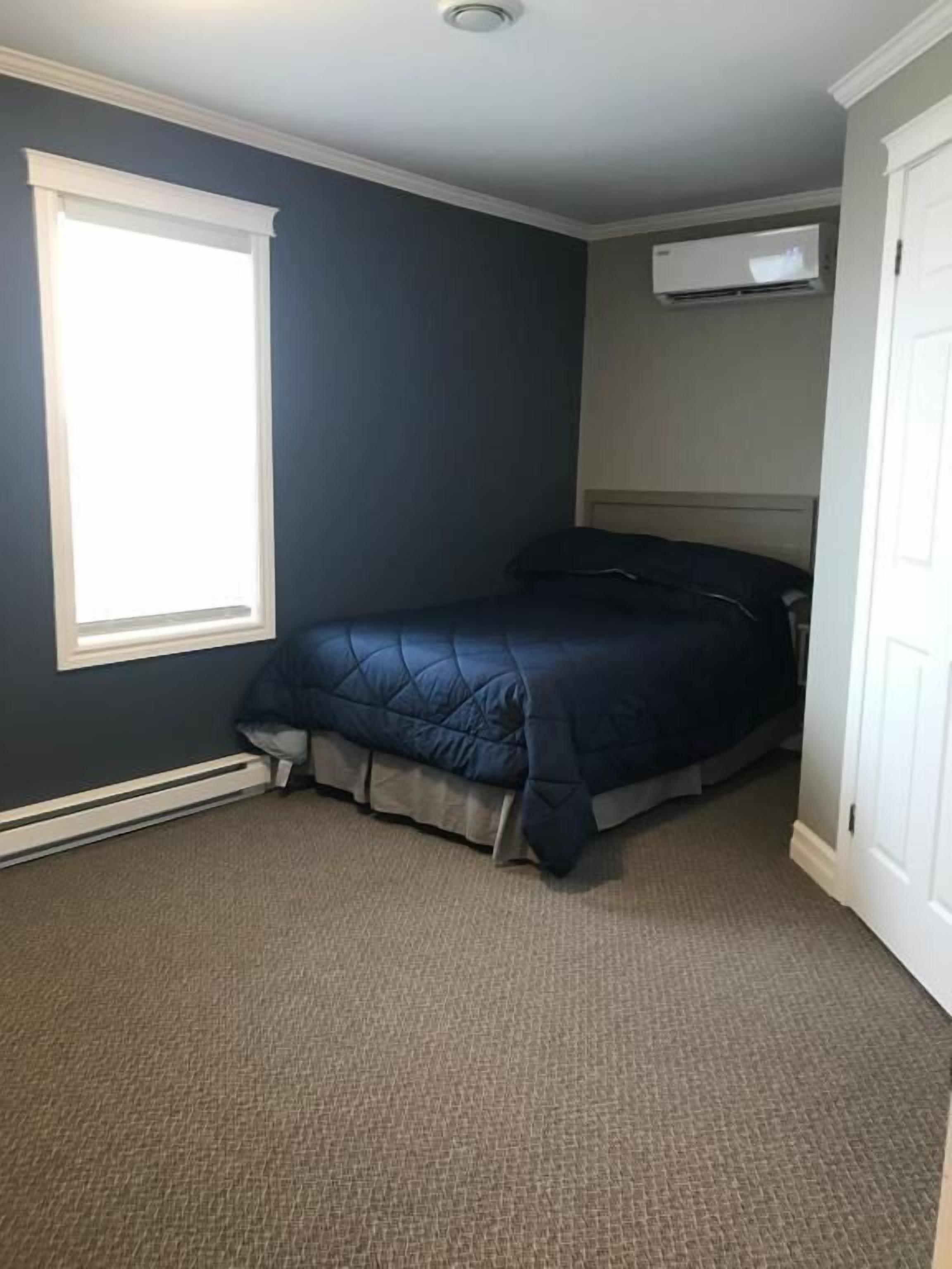 A bedroom with a bed, a window, and an air conditioning unit.