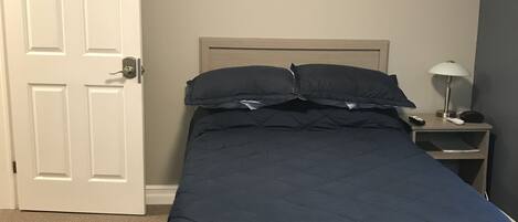 Ein Schlafzimmer mit einem Bett, einem Nachttisch, einer Lampe und einer Tür.