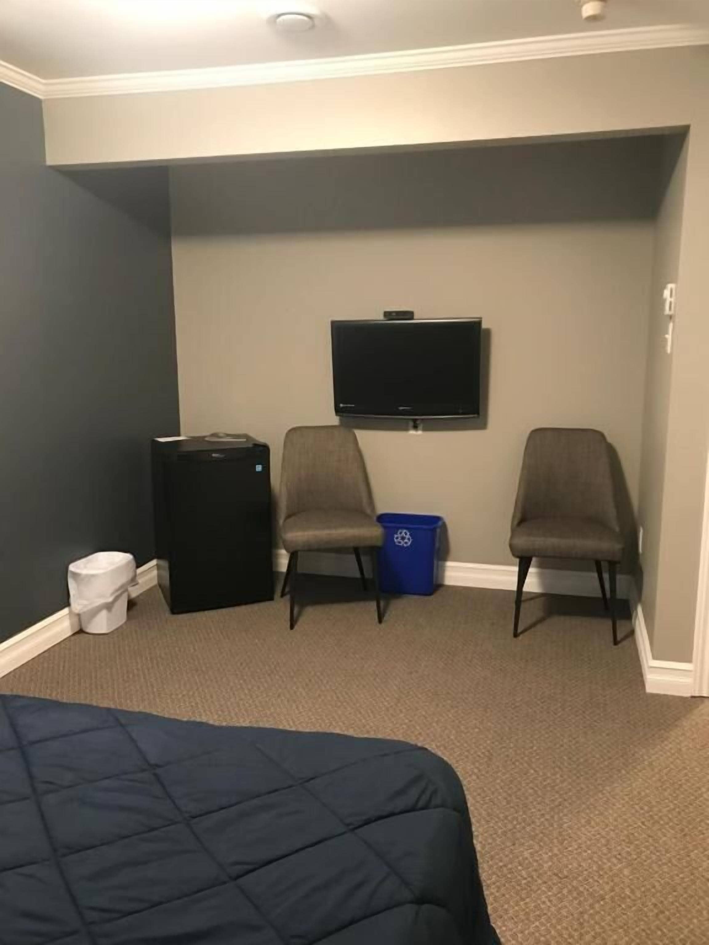 Ein Hotelzimmer mit Bett, Schreibtisch, Stuhl, Fernseher und Mülleimer.