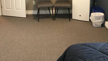 A room with a door, two chairs, a small white cabinet, a television, and a trash bin.