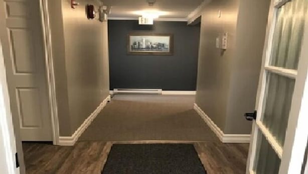 A hallway with a dark carpet, wooden flooring, and a framed picture on the wall. - Stanley House (Clarenville)