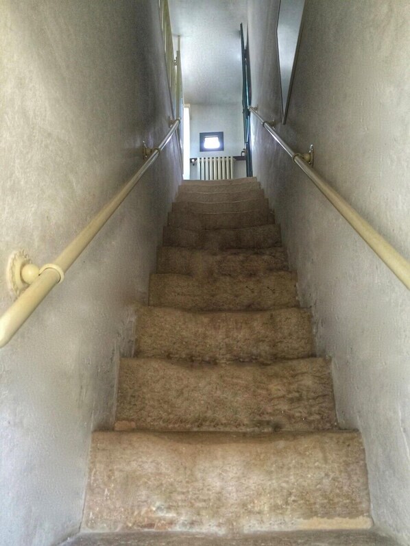 Una escalera con peldaños alfombrados, barandales de metal y un radiador en la parte superior.
