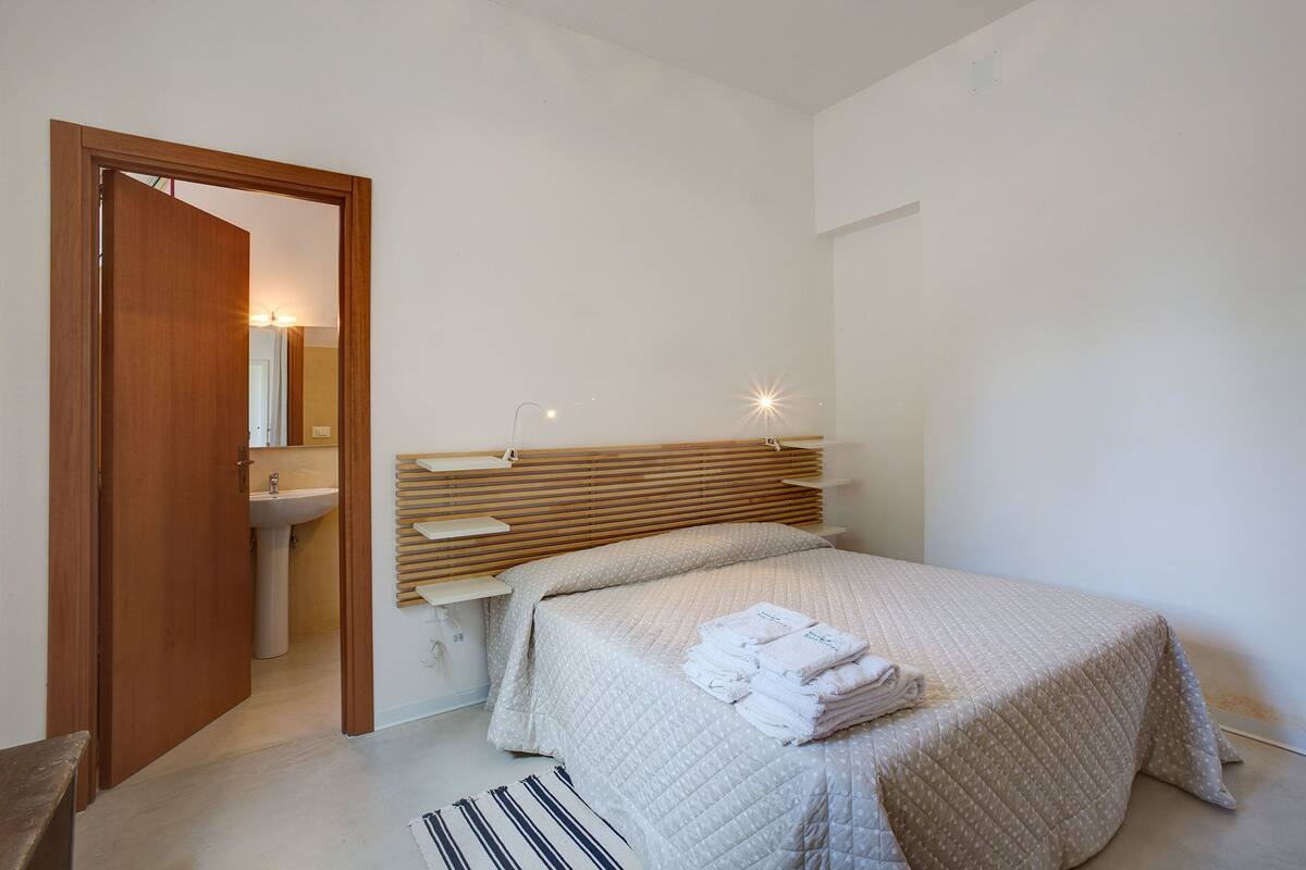 A bedroom with a bed, bedside tables, a nightstand, a mirror, and a door.