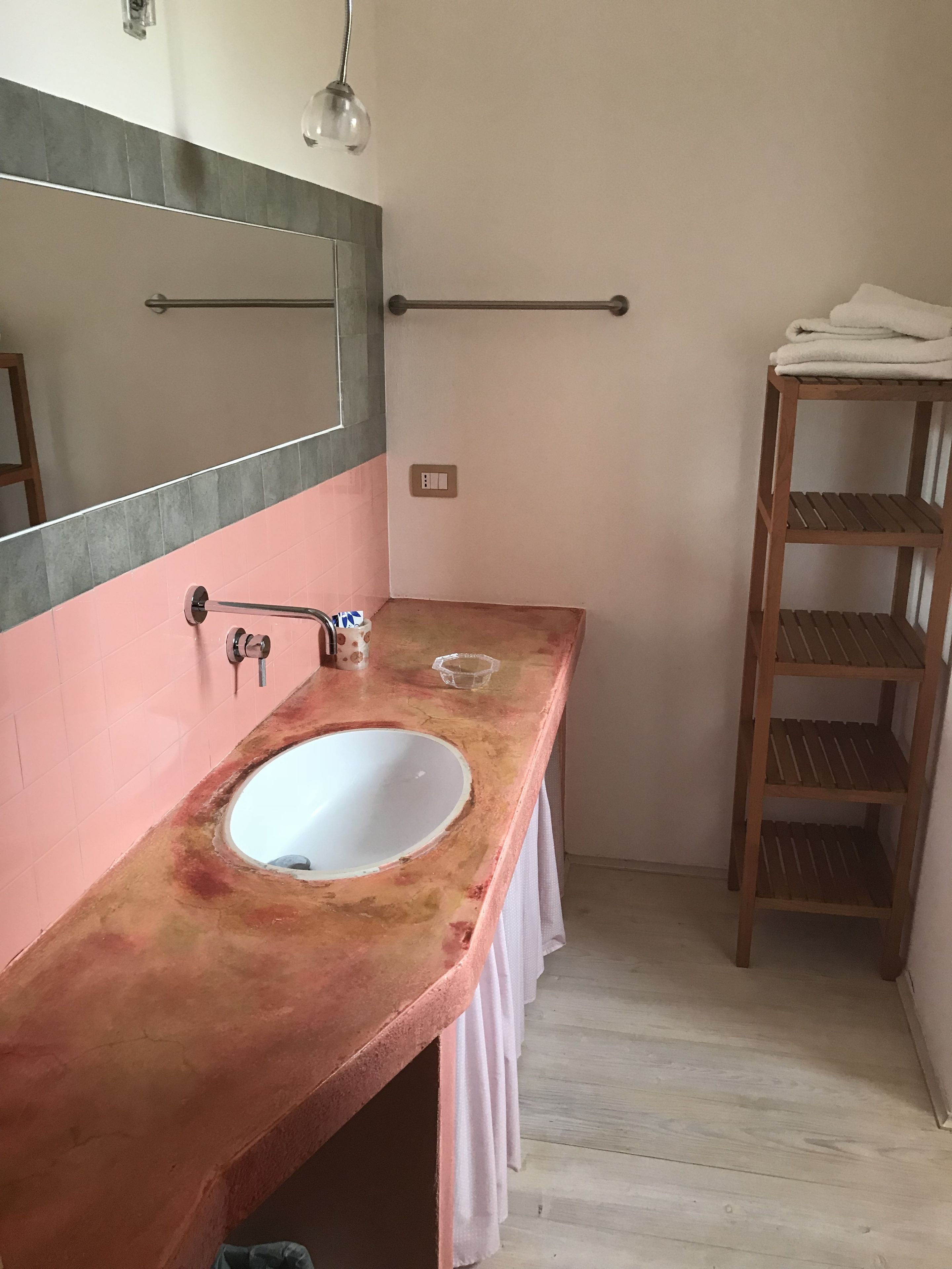 A bathroom with a pink and gray tiled wall, a white sink, a wooden shelf, and a towel rack.