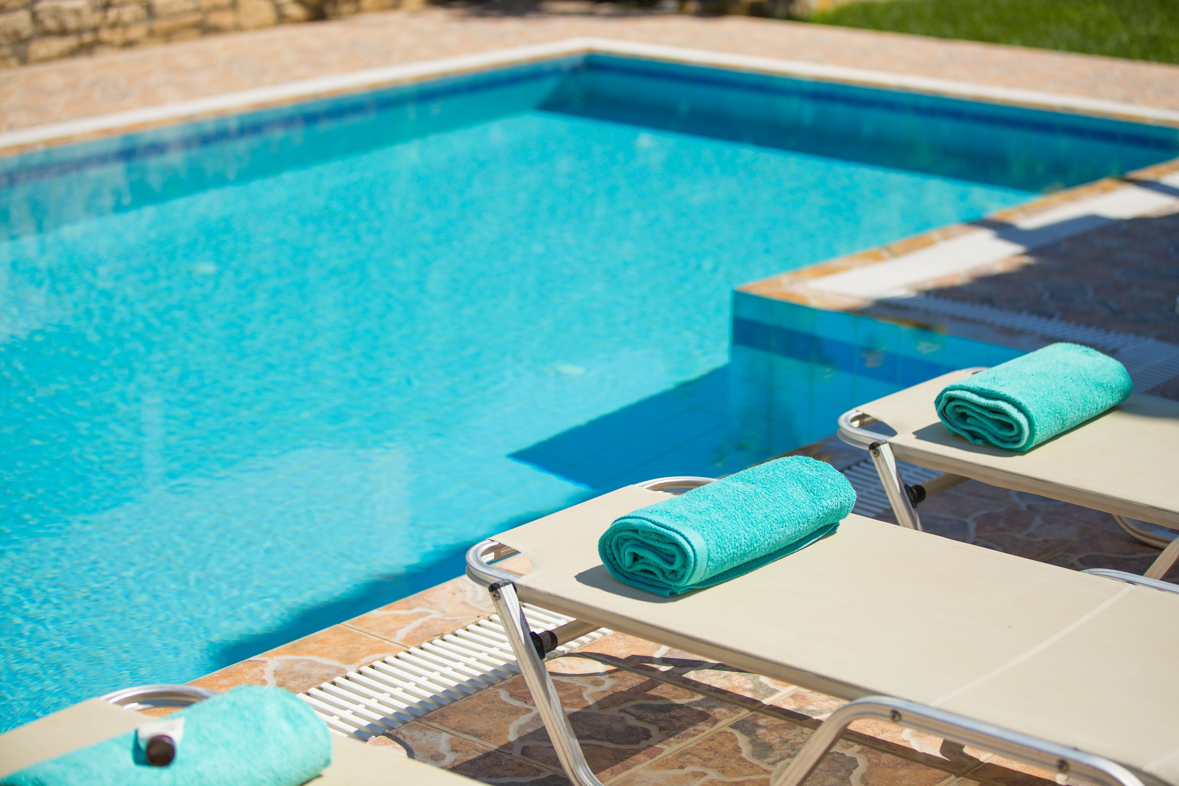 A swimming pool with clear blue water, a tiled deck, and two lounge chairs with towels.