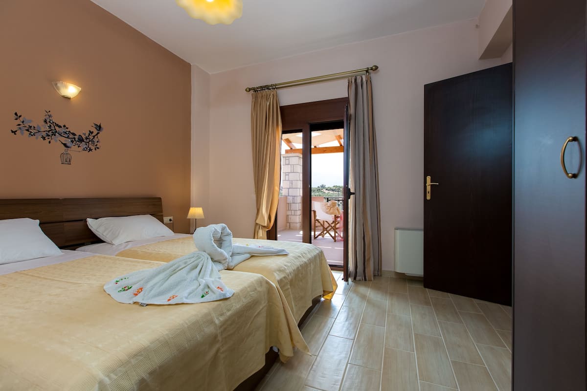 A hotel room with two beds, a wooden headboard, a decorative wall piece, and a view of the outdoor area through a glass door.