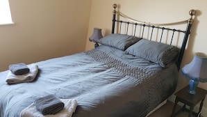 A neatly made bed with a grey comforter, two pillows, and folded towels on the side. - Apartment 9 Robertson Villas (Rochester)