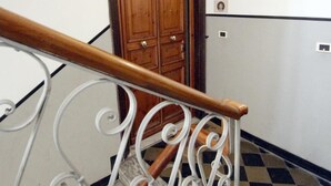Un escalier doté d’une main courante en bois et de balustrades en métal blanc, menant à une porte en bois surmontée d’un sol à carreaux noirs et blancs.