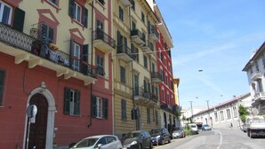 Une rangée d’immeubles à plusieurs étages dotés de balcons, des voitures garées et un ciel dégagé.