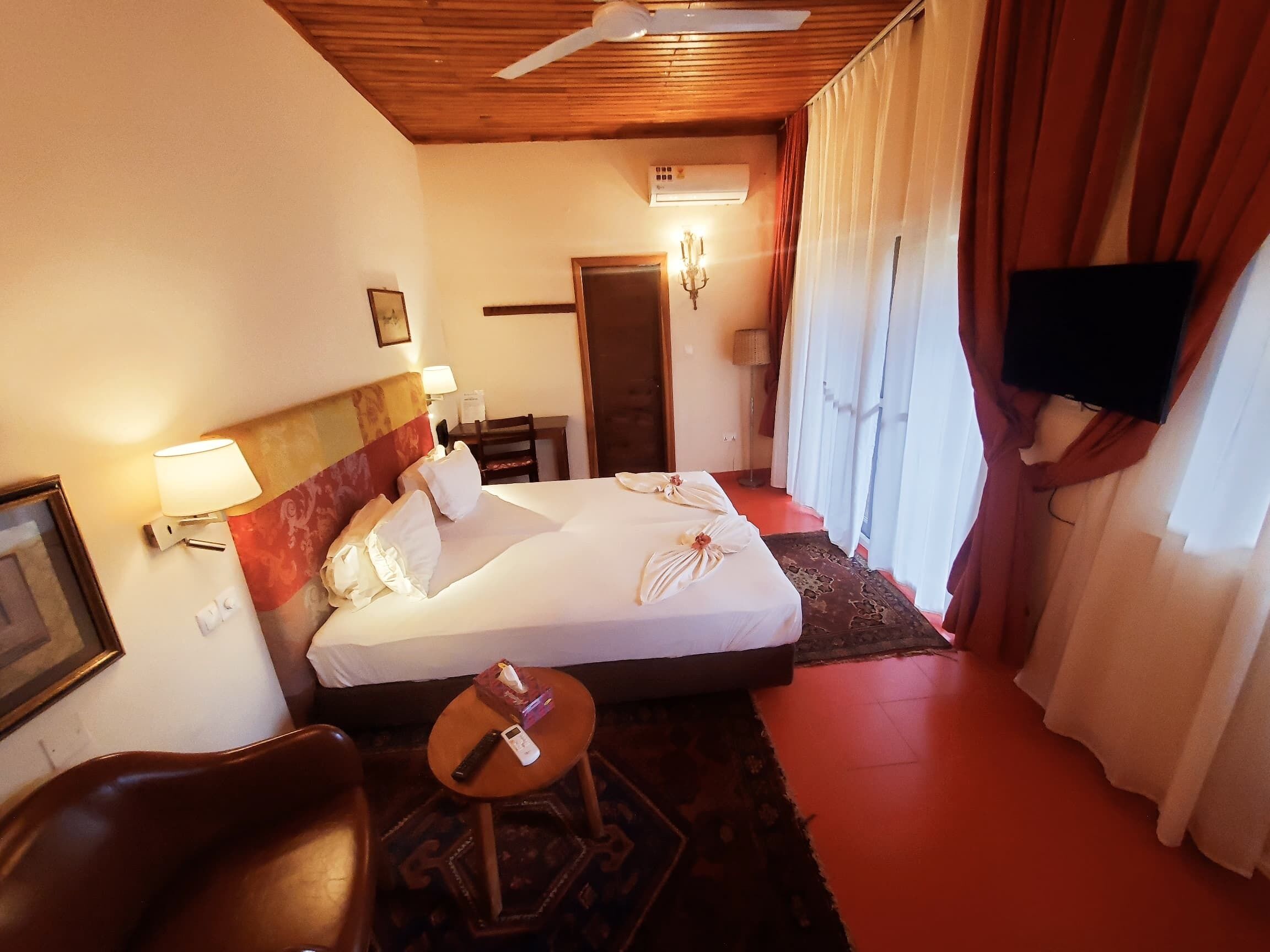 Habitación de hotel con una cama, escritorio, silla, televisor y ventilador de techo.