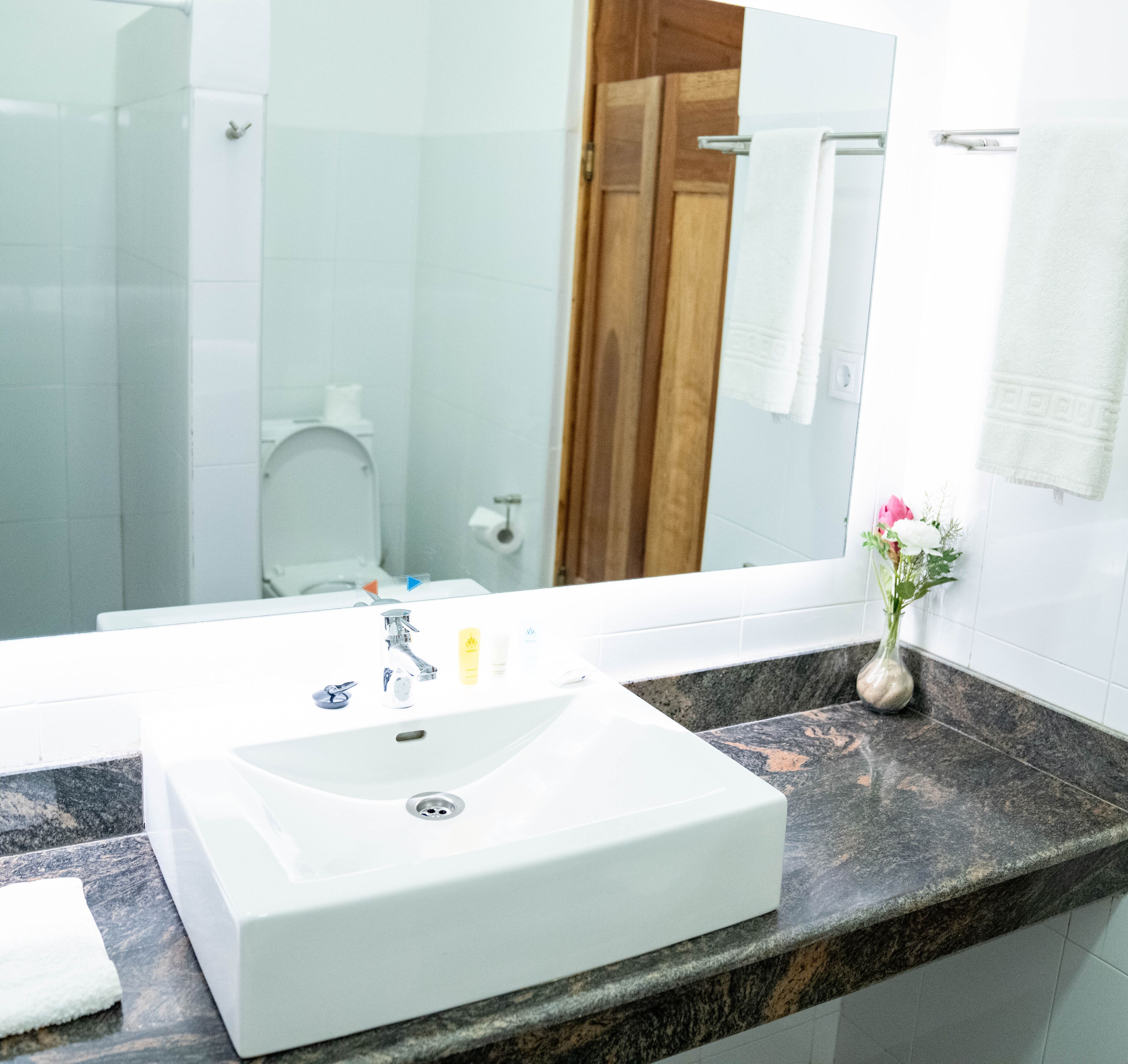 A bathroom with a white sink, a mirror, a marble countertop, and a vase with flowers.