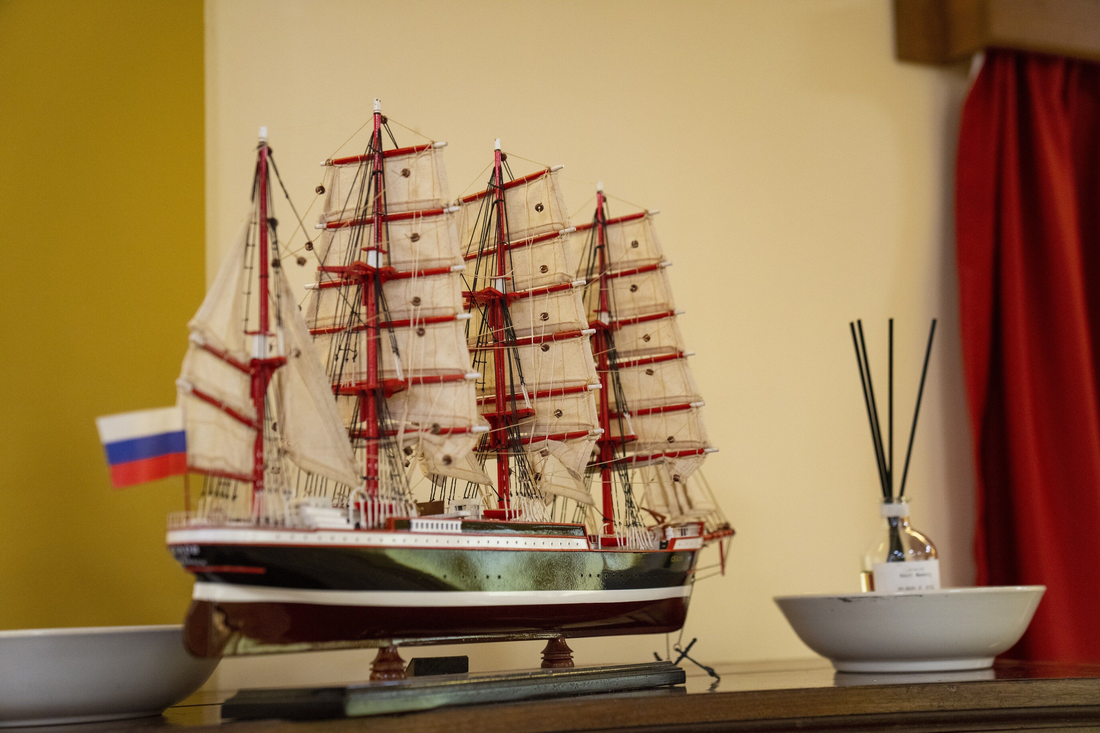 Un modelo de barco en una mesa, con un cuenco pequeño y una botella de palitos de incienso a su lado.
