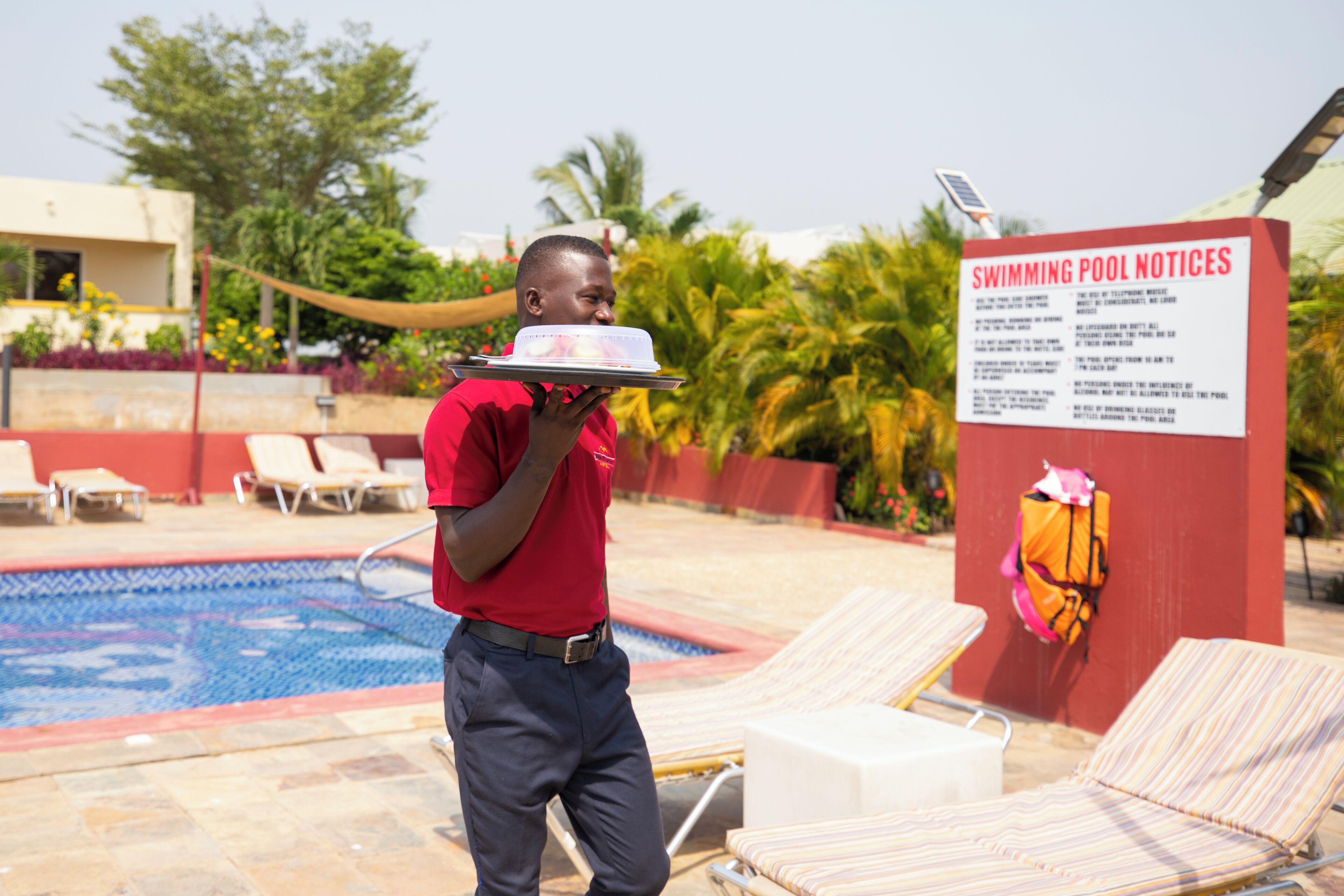 A swimming pool area with lounge chairs and a signboard with swimming pool notices.