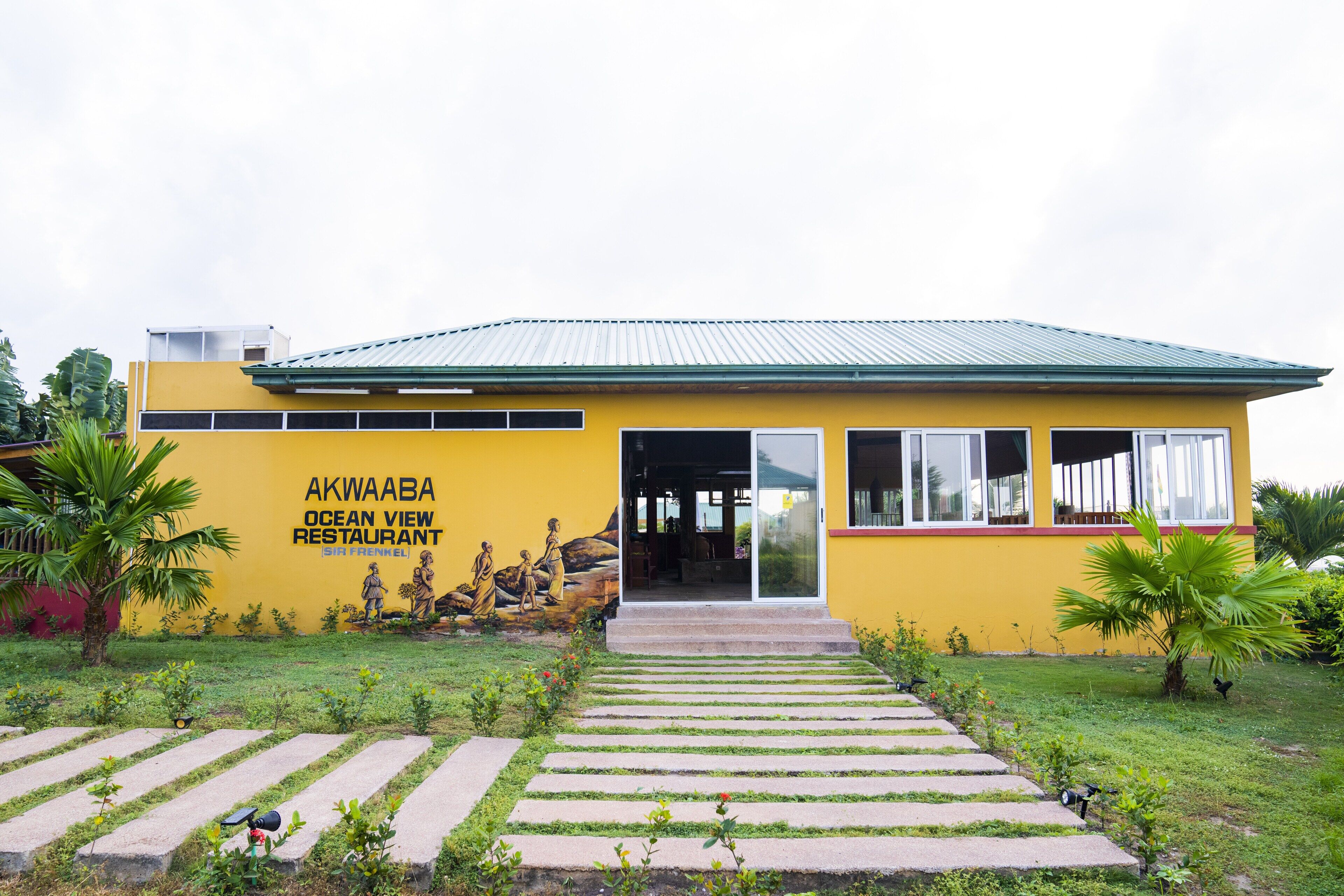 A yellow building with the sign "AKWAABA OCEAN VIEW RESTAURANT" and a pathway leading to the entrance.