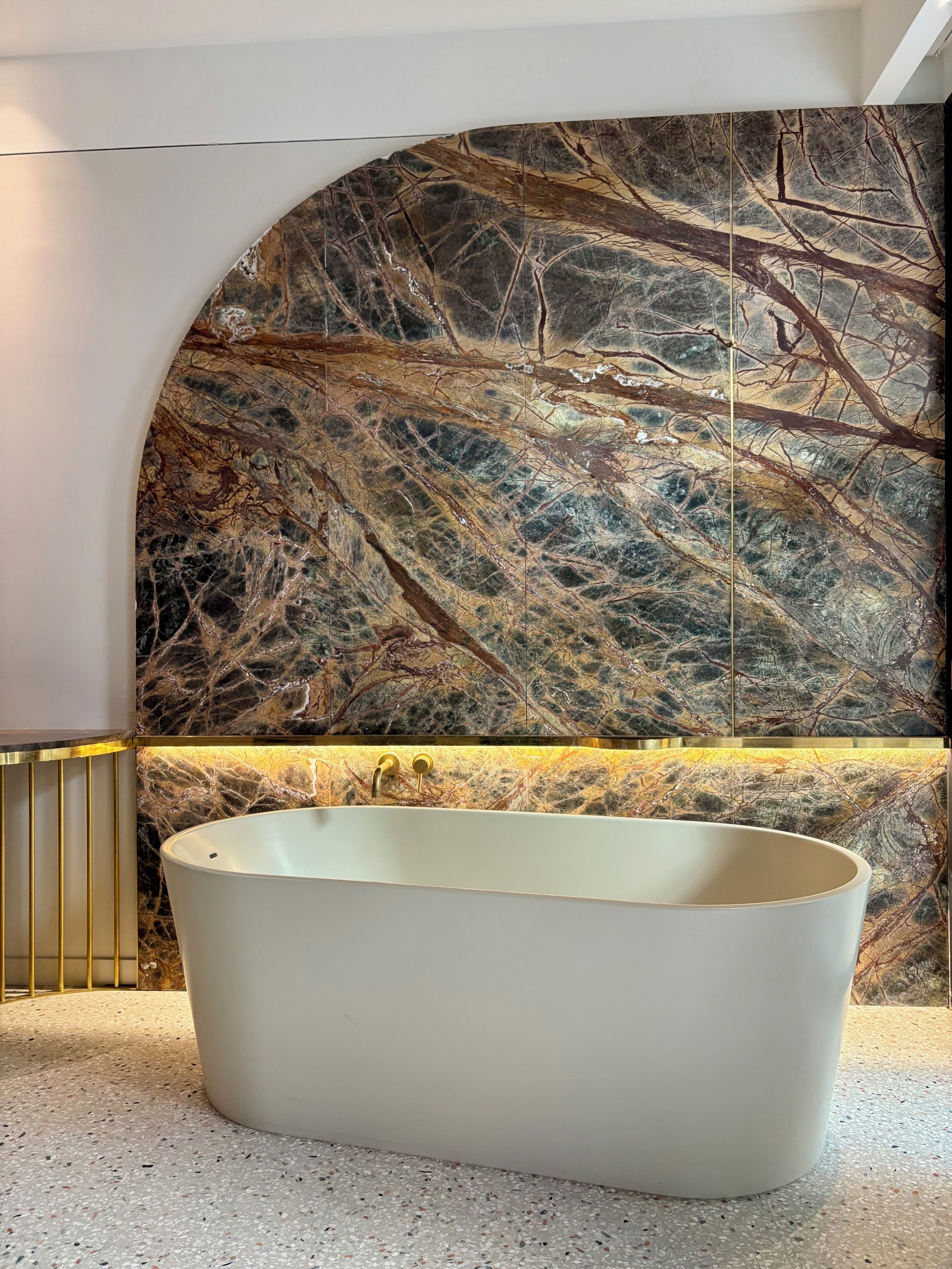 A modern bathroom with a freestanding bathtub, a marble backsplash, and a gold-framed vanity.