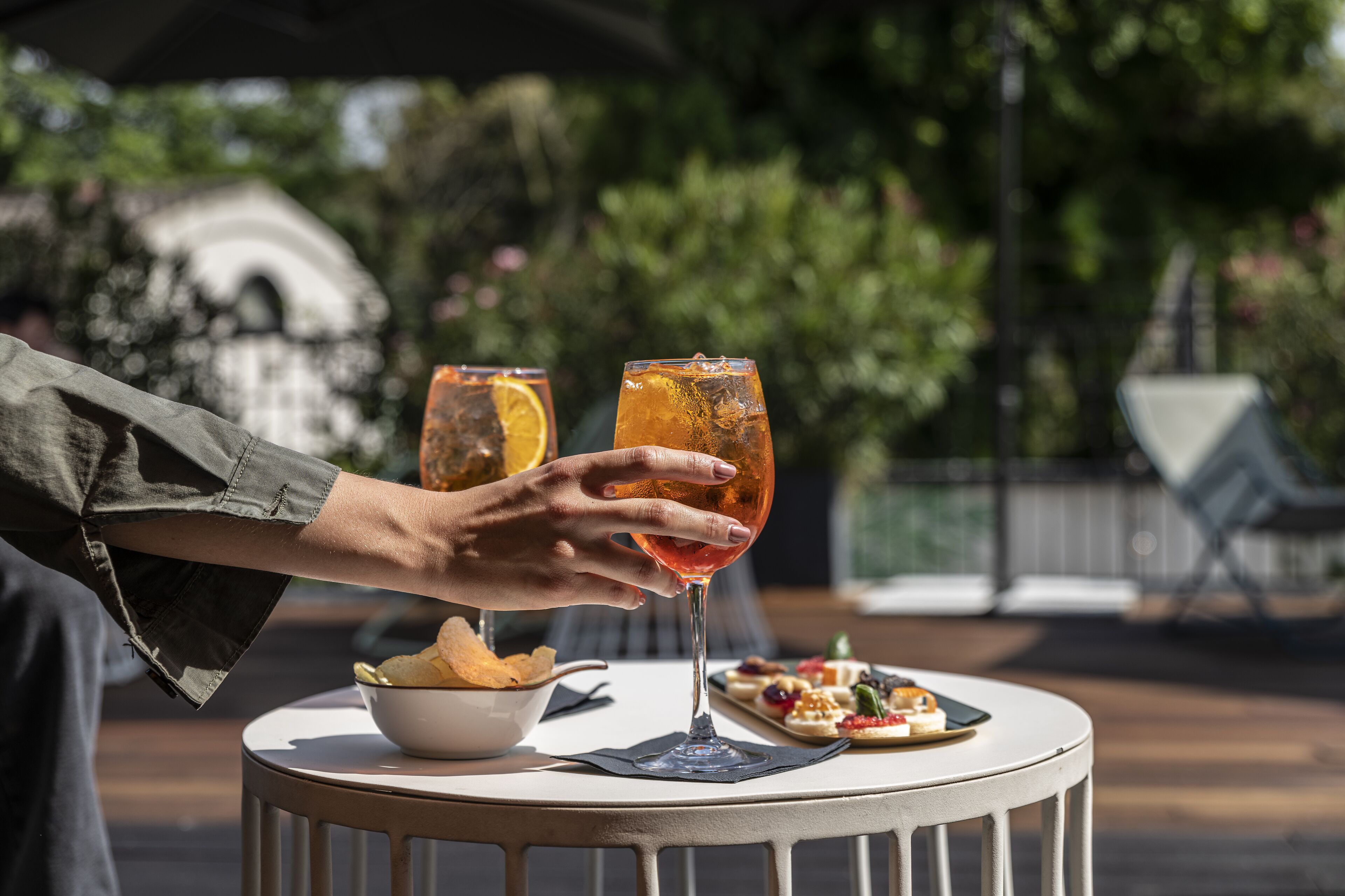 A person holding a glass of drink at a table with a bowl of chips and a plate of appetizers.