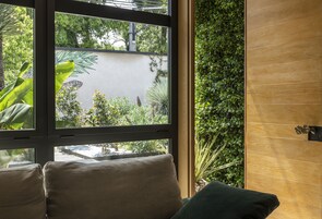 A room with a large window overlooking a garden, a wooden wall, and a cushioned seating area.
