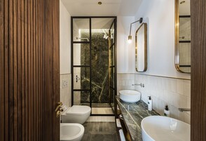 Een moderne badkamer met een douchecabine van glas, twee wastafels en een badkamermeubel met een marmeren werkblad.