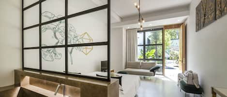 A modern bathroom with a large bathtub, a glass partition with artwork, and a view of a garden through a large window.