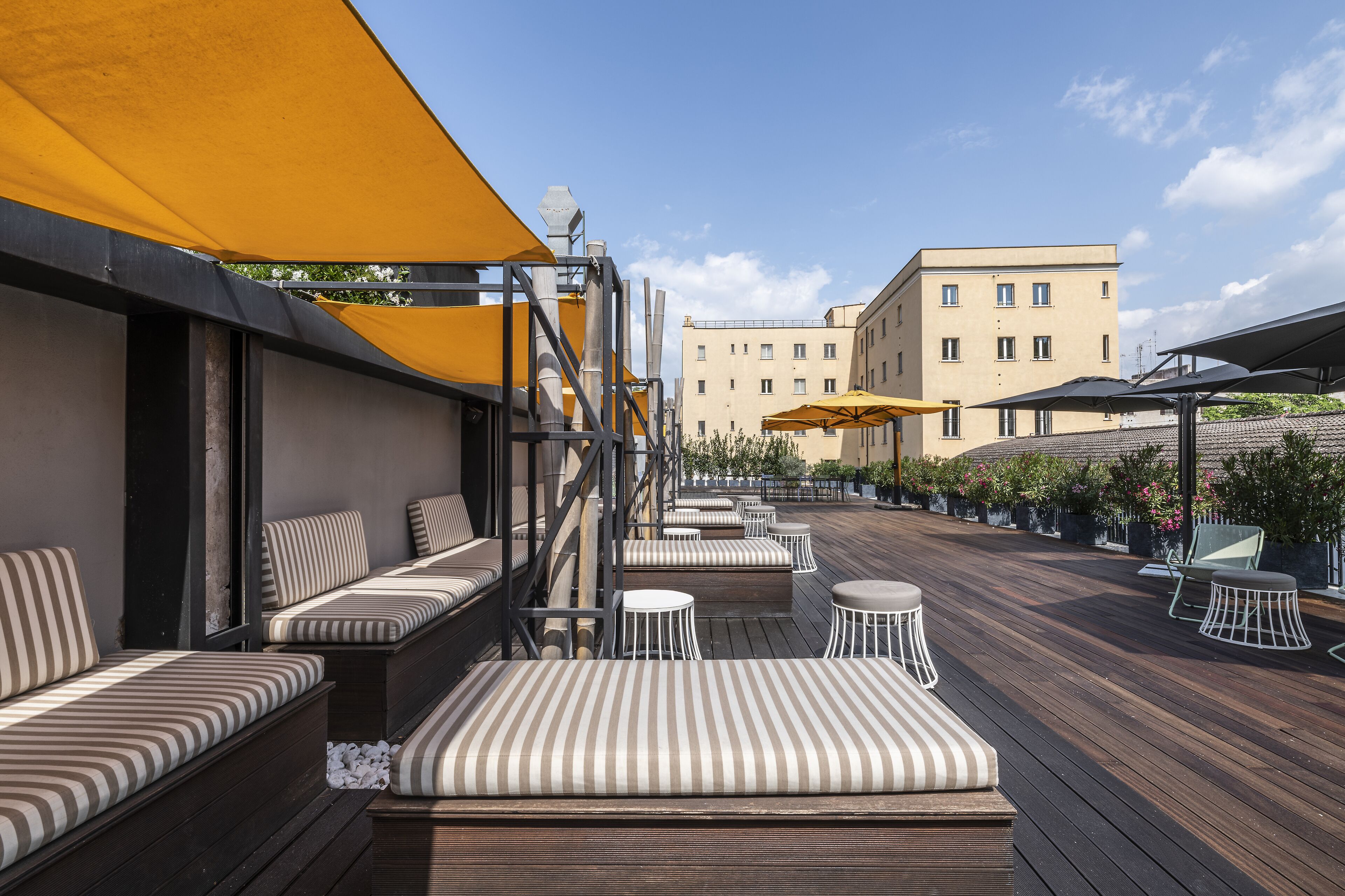 Una terraza en la azotea con zonas de estar, sombrillas y vistas a un edificio al fondo.