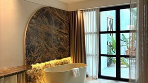 Une salle de bain moderne avec une baignoire sur pieds, un mur d’accent en marbre et une grande fenêtre agrémentée de rideaux.