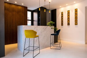Un'area reception con un bancone in marmo, due sgabelli da bar, illuminazione a sospensione e una parete con opere d'arte incorniciate.