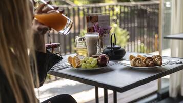 A table with a glass of orange juice, a pitcher of milk, a teapot, and plates of grapes and croissants.