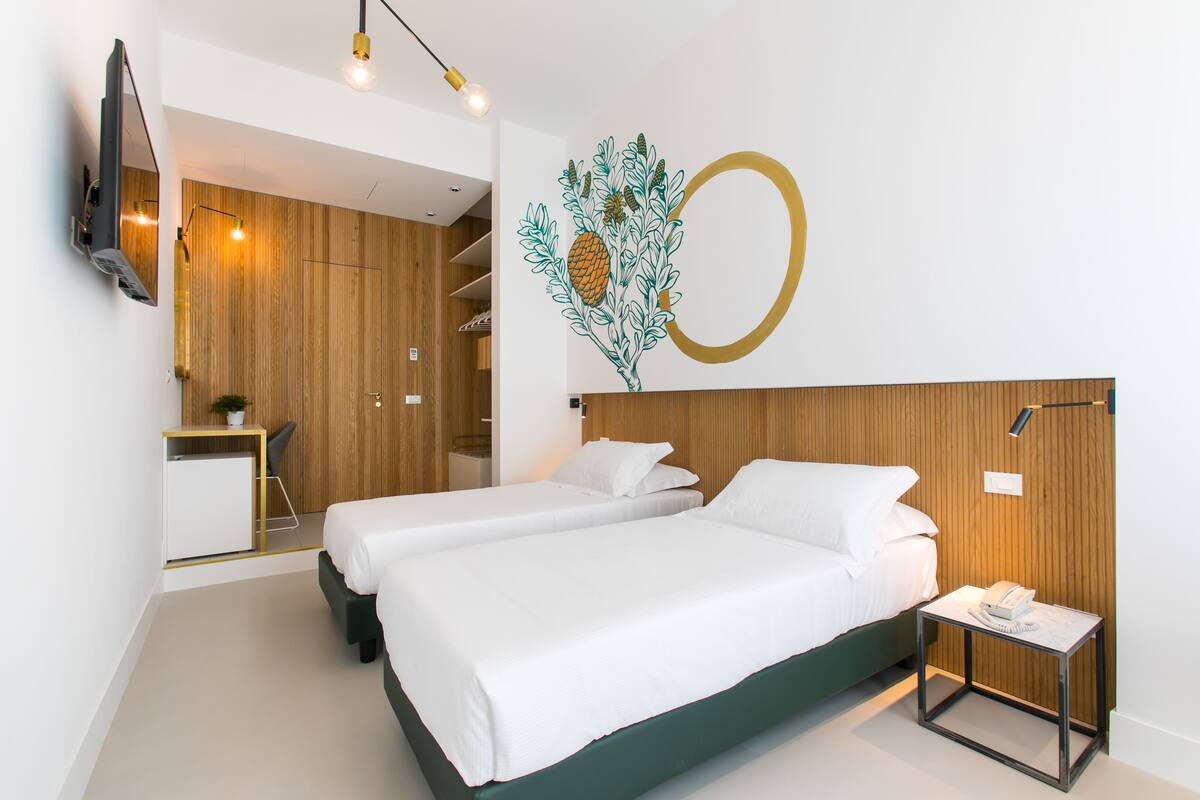 Una habitació d'hotel moderna amb dos llits, un escriptori, un televisor i una obra d'art decorativa a la paret.