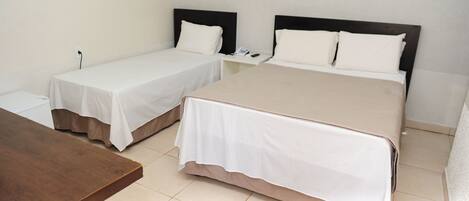 Habitación de hotel con dos camas individuales y una cama doble, una mesa de madera y una pared blanca.