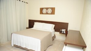 Habitación de hotel con cama, mesita de noche de madera, escritorio blanco y una obra de arte en la pared.