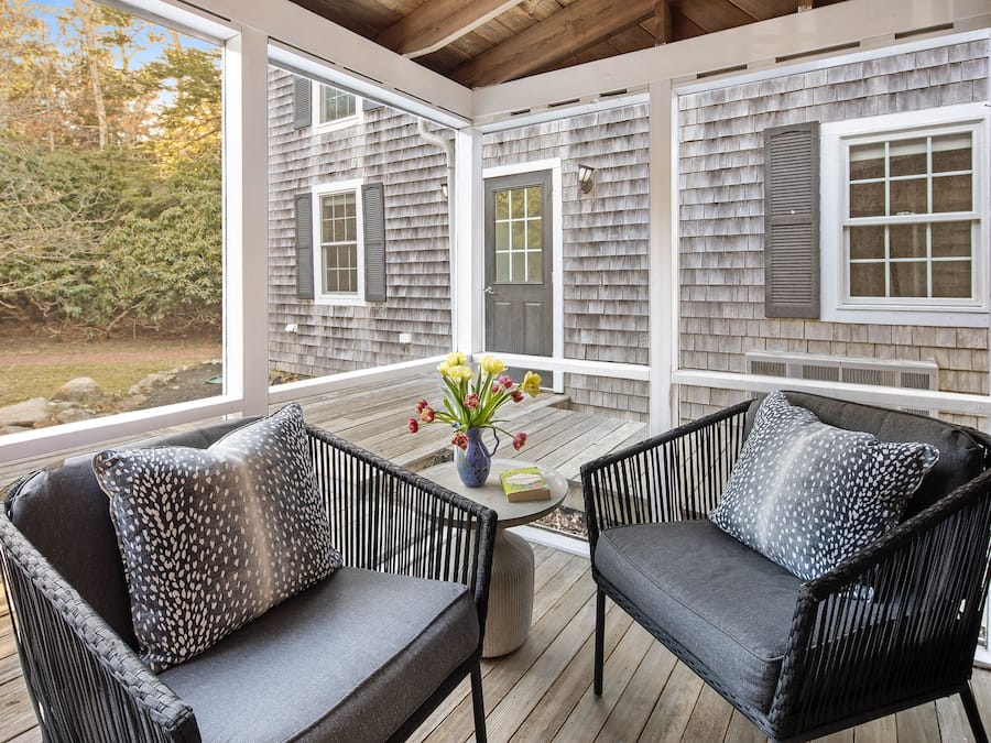A covered porch with wicker furniture and a vase of flowers.