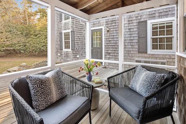 A covered porch with wicker furniture and a vase of flowers.